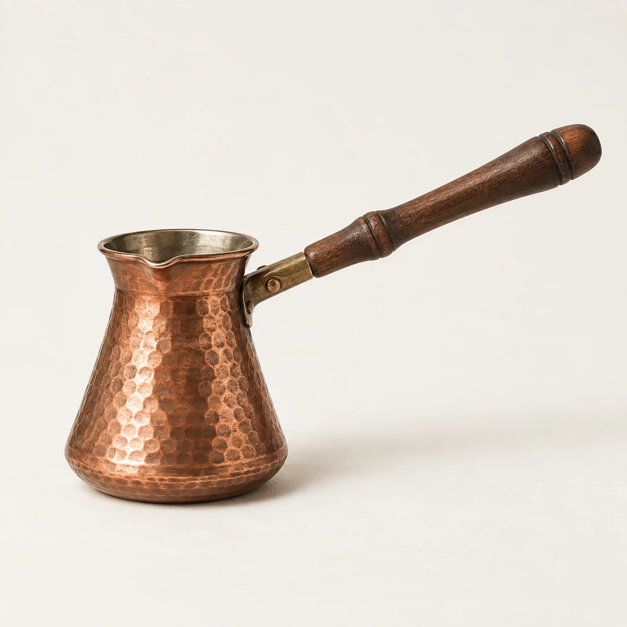 Cafetera de mango largo. Imagen ilustrativa generada por IA; materiales: cobre y madera.